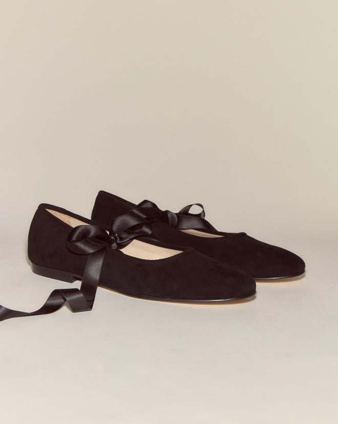 The Musette Flats - Black are vintage-inspired ballet flats in black suede with elegant black satin ribbon laces, displayed on a neutral background.