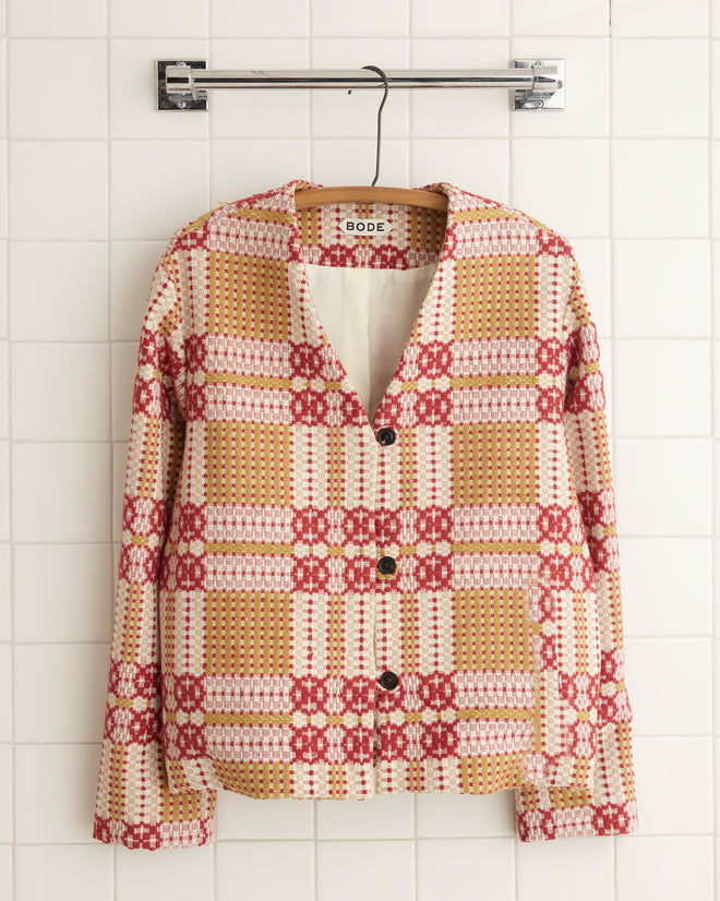 A vibrant Nandina Coverlet Jacket - 5, featuring floral patterns similar to an antique coverlet, is displayed on a hook against a tiled wall.