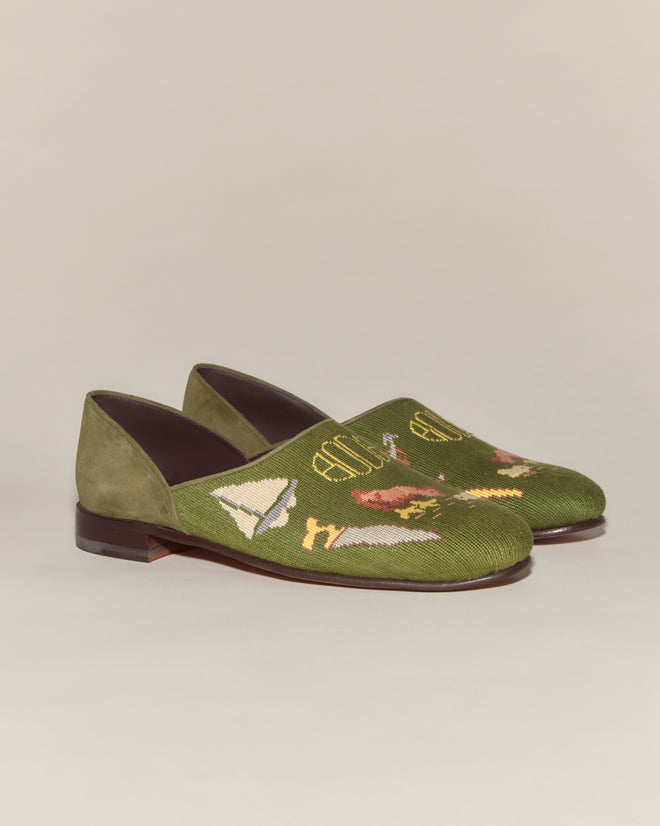 A pair of Needlepoint House Shoes in green, made in Italy, featuring embroidered designs such as a paper airplane and colorful motifs for a unique slipper style.