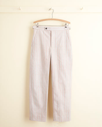 The Neon Tube Trousers - 28, featuring beige and pink stripes made from strip-woven fabric, hang on a wooden hanger against a light-colored wall.