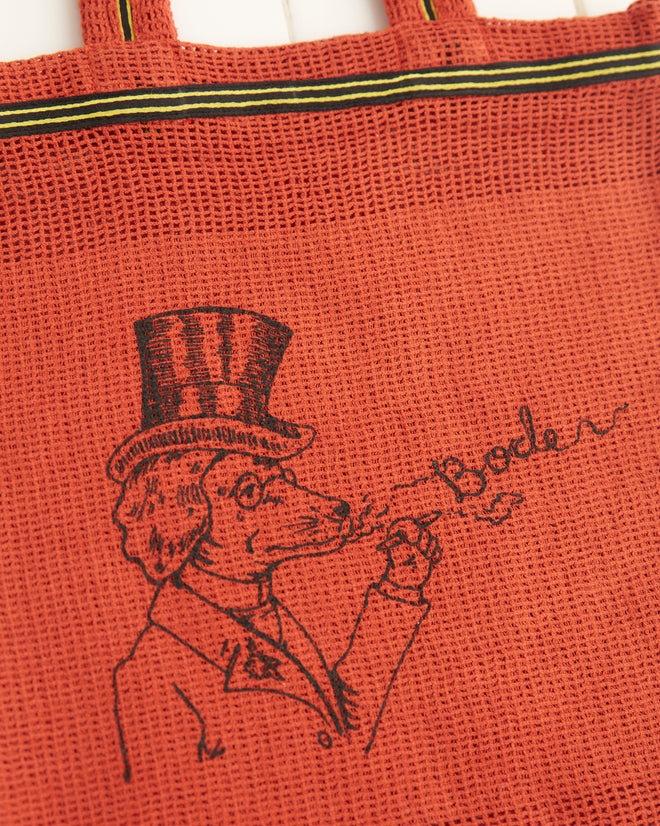 Orange Netting Tote featuring a whimsical dog illustration with a person in a top hat blowing bubbles, with 