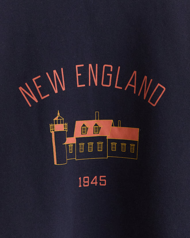 The New England Crewneck - Midnight is a navy blue 100% cotton shirt featuring “NEW ENGLAND,” a lighthouse, house graphic, and “1945” in red and yellow—ideal for fans of classic screen-printed styles.