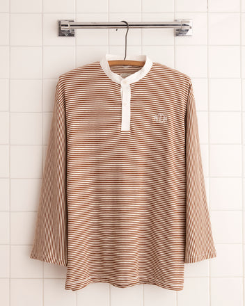 Newton Stripe Polo in brown and white cotton with long sleeves, displayed on a hanger against a tiled wall.