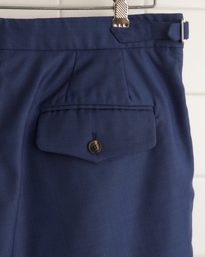 The Night Blue Wool Shorts - 34, crafted from men's suiting fabric for a perfect blend of style and durability, hang on a wooden hanger against a white tiled wall.