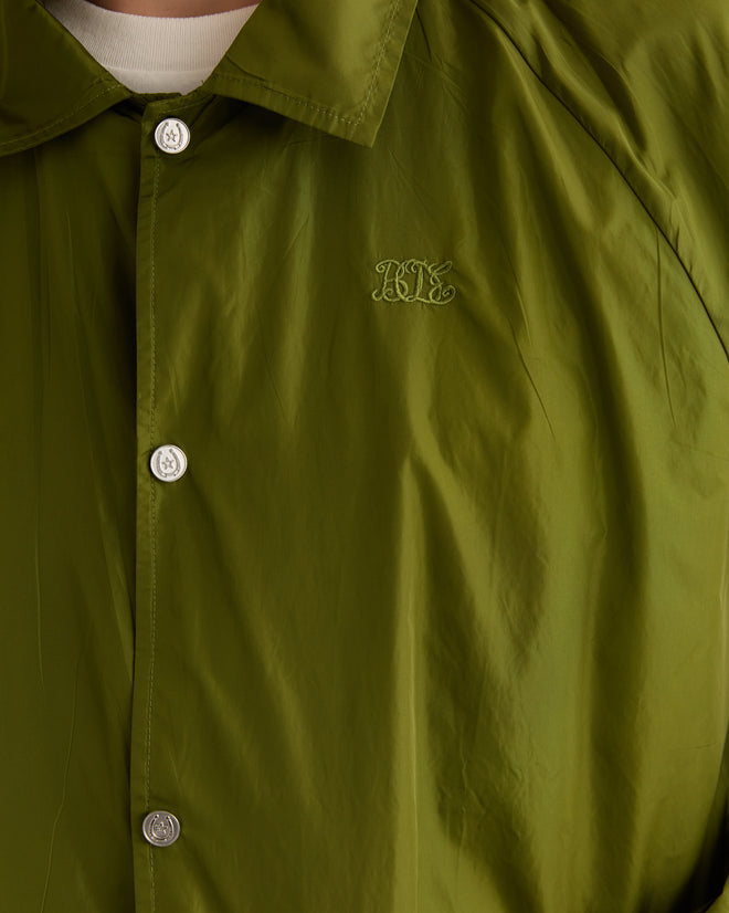 Close-up of an olive nylon track jacket featuring the "KL" Bode monogram embroidered on the chest, blending elegance with casual flair.