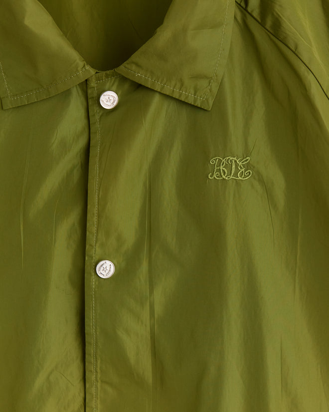 Close-up of the olive Nylon Track Jacket adorned with Bode monogram embroidery on the chest, highlighted by glossy enamel snap buttons.