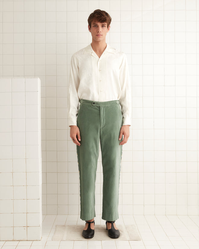 A person in a white shirt and Oberon Floral Trousers, inspired by 1930s-1940s fashion, stands against a tiled wall.