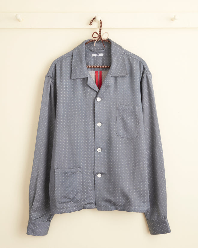 The Omura Diamond Long Sleeve Shirt - M/L, featuring a unique small dotted pattern in gray, hangs on a hook against a light-colored wall.