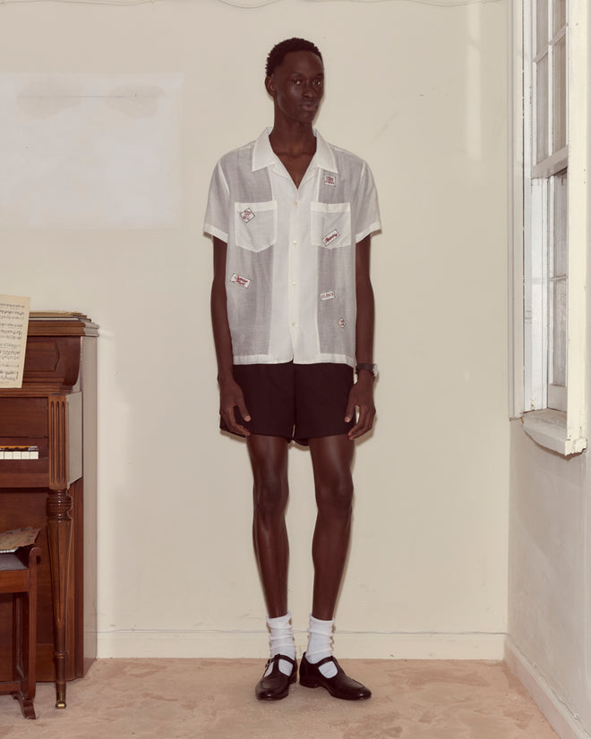 A man wearing the On Air Short Sleeve and black shorts stands indoors by a piano and a window, looking forward.