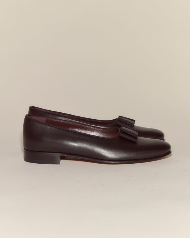 A pair of Opera Pumps, crafted from black Napa leather with low heels and decorative bows, inspired by classic men's evening dress slippers, is displayed on a neutral background.