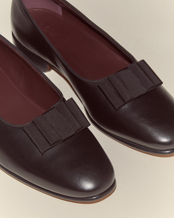 A pair of Opera Pumps—black Napa leather flats with pleated ribbon bows on the toes, inspired by classic Opera Pump designs—photographed on a light background.