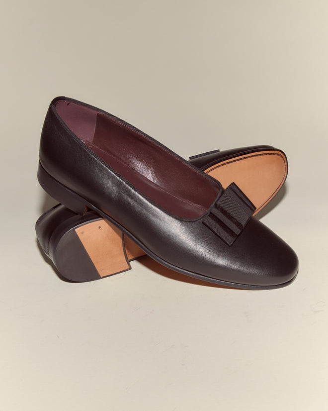 Opera Pumps: Black Napa leather loafers with low heels and decorative bows, inspired by classic men's evening dress slippers, shown on a neutral background.
