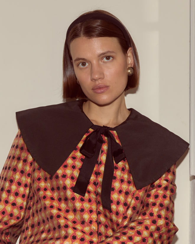 Woman with straight brown hair wearing the Orana Collar Jacket, featuring a 1960s print and a large black collar, looking at the camera.