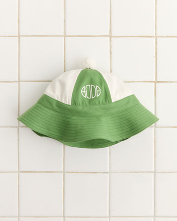 The Paneled Grandfather Hat in green/white, crafted from 100% cotton with Bode embroidery, is showcased on a tiled background. Ideal for that college reunion hat vibe.