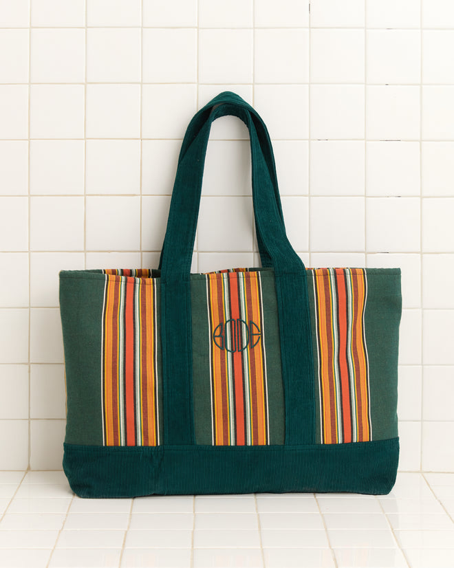 The Parakeet Stripe Tote is a striped canvas bag with corduroy handles, green trim, and an embroidered Bode logo, shown against a white tiled background.