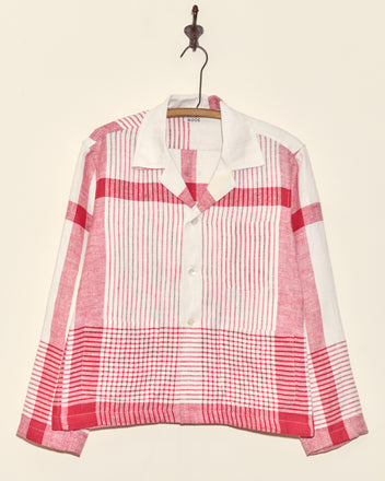 The Park Stripe Long Sleeve Shirt - S, featuring red and white plaid and a unique charm, hangs on a wall hook.