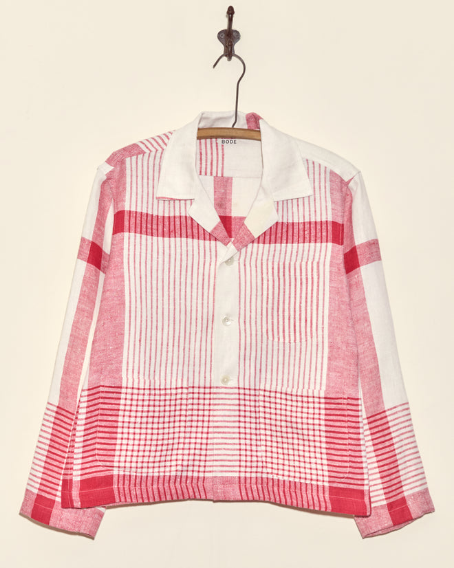 The Park Stripe Long Sleeve Shirt - S, featuring red and white plaid and a unique charm, hangs on a wall hook.