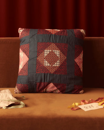 The charming Parquet Inlay Pillow adorns the brown couch, its red, blue, and brown patterns evoking an air of nostalgia. Scattered ribbons rest nearby, complementing the vintage calico prints that add character to this delightful piece of home goods.