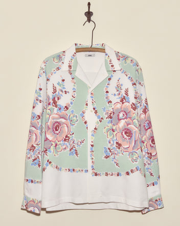 The Pastel Bouquet Long Sleeve Shirt - L/XL, featuring a unique pastel floral print, hangs on a hook against a cream wall, bringing a touch of midcentury charm.