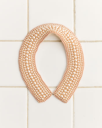 The Pearl Collar, a 1960s-inspired necklace adorned with pearl beads, is elegantly showcased on a tiled surface.