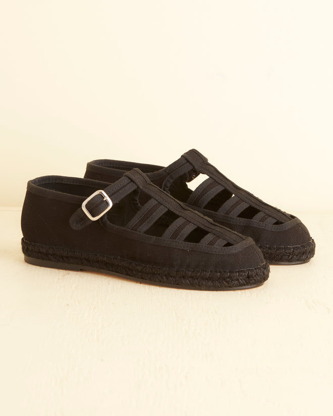 The Peggy Espadrilles - Black, featuring a pair of black, closed-toe espadrilles with a buckle strap, multiple cutouts, and a braided jute sole, placed on a light surface: the perfect summer shoes.