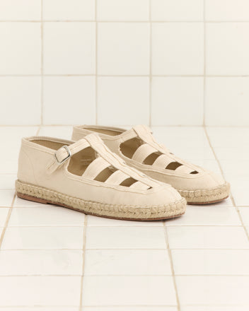 Peggy Espadrilles - Natural, featuring a canvas upper with cutout sides, buckle straps, and a classic jute sole, are shown on a white tiled surface.
