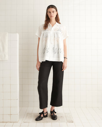 Person wearing a Petticoat Short Sleeve Shirt, a white 100% cotton button-up blouse with a lace pattern, and black pants, standing in front of a tiled wall.