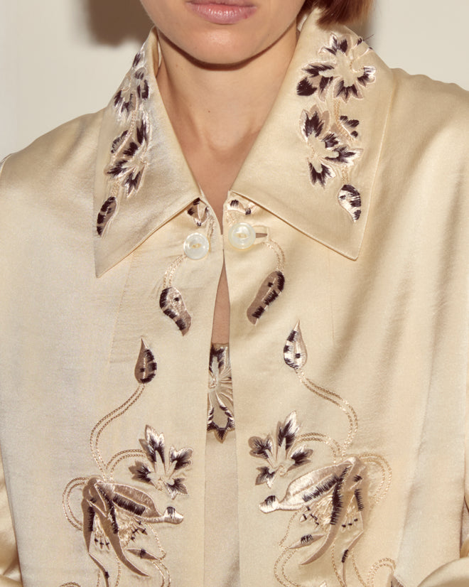 Close-up of the Phantasm Fringe Jacket, featuring cream satin fabric with Victorian embroidery and large pearl buttons, worn by a person.