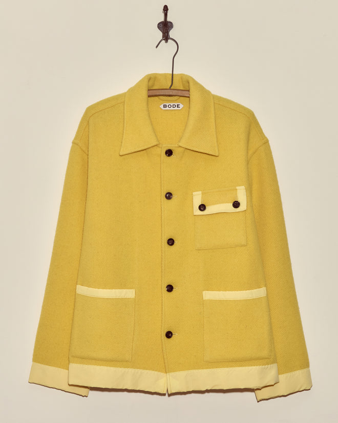 Phosphorus Jacket - M: Yellow midcentury wool jacket with cream trim, front pockets, and a collar, displayed on a hook against a wall.