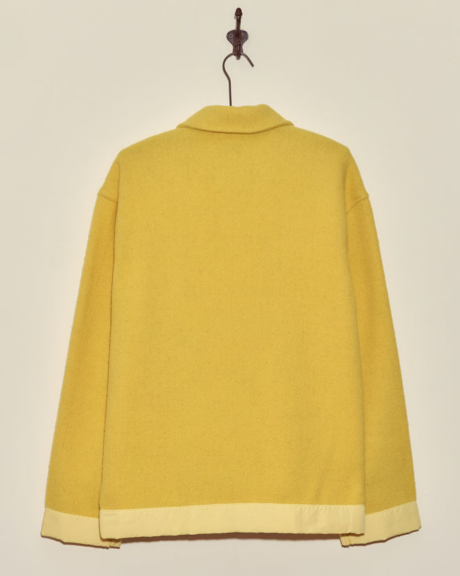 The Phosphorus Jacket - M, featuring a bright yellow color, collar, and light trim, hangs on a hook against a plain off-white wall.