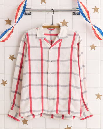 The Picnic Check Shirt - M/L features unique white fabric with red and gray plaid checks, displayed on a hanger among star and streamer decorations—a standout vintage textile find.