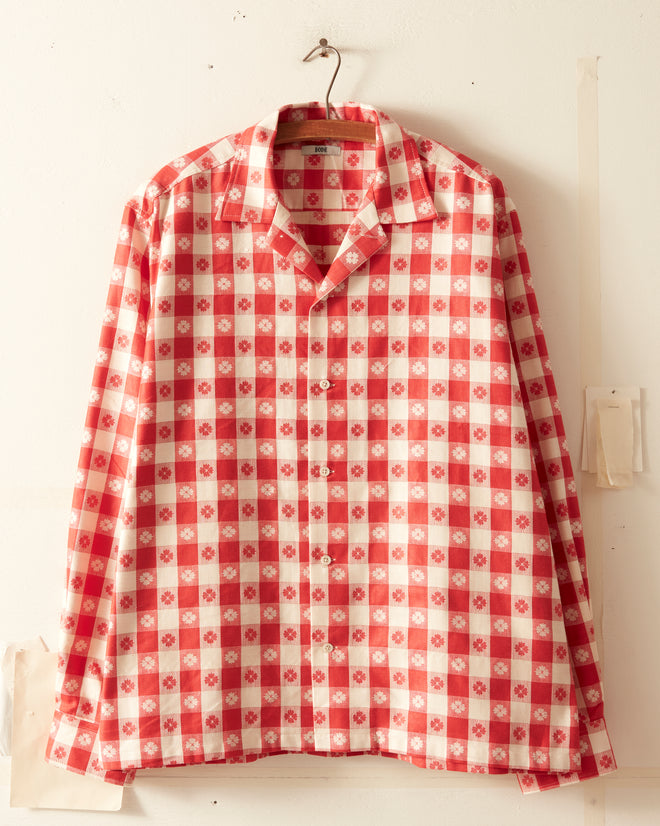 The PICNIC PARTY SHIRT, a red and white checkered long-sleeve shirt perfect for a picnic or party, is displayed on a hanger against a plain white wall.