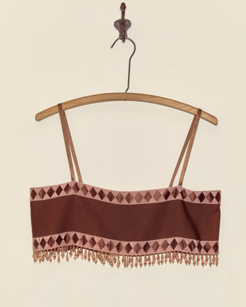 The Pierrot Bead Bra - S is a brown cropped top with thin straps, geometric trim, Staron jacquard ribbon, and beaded fringe, displayed on a wooden hanger—a unique statement piece.