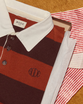The Pine Stripe Polo, crafted from virgin wool, is presented in a box with tissue paper and a red striped bag on a brown surface.