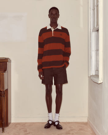 A person in a Pine Stripe Polo, black shorts, white socks, and black shoes stands indoors by a window.