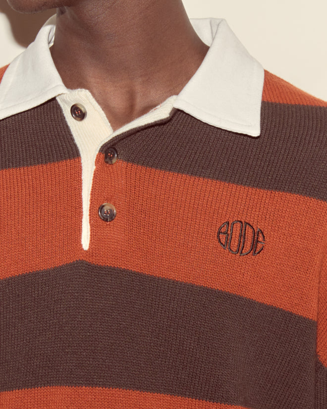 A person wearing the Pine Stripe Polo—an orange and brown striped rugby with a white collar and 