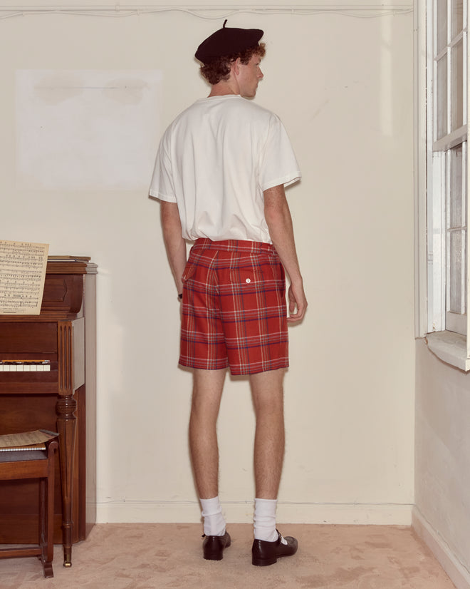 A man in a white shirt, Gable Plaid Shorts, beret, and loafers stands facing away in a room at Camp Onibar.
