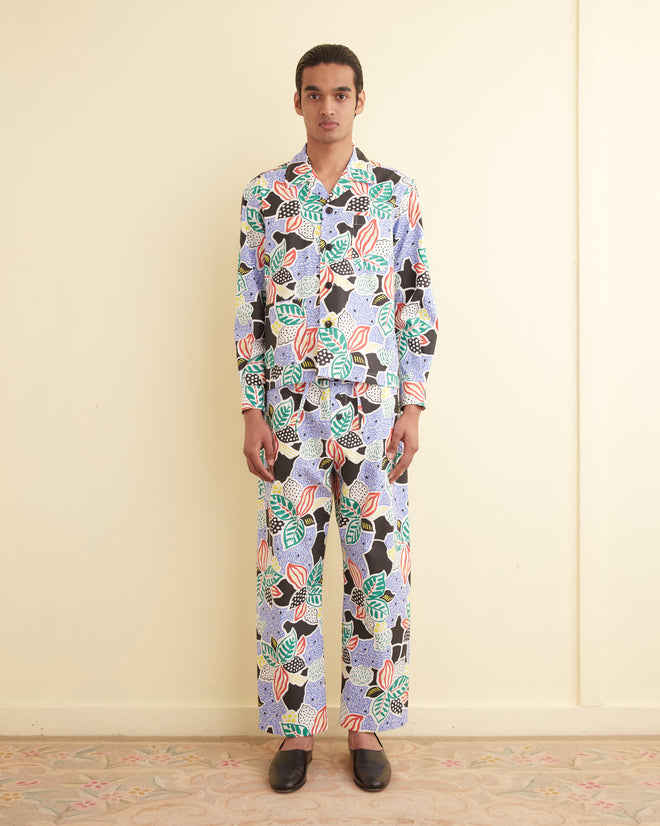 In a room with light walls and floors, a person wears the unique Plantain Jazz Long Sleeve Shirt - M, showcasing an oversized botanical pattern inspired by midcentury French yardage.