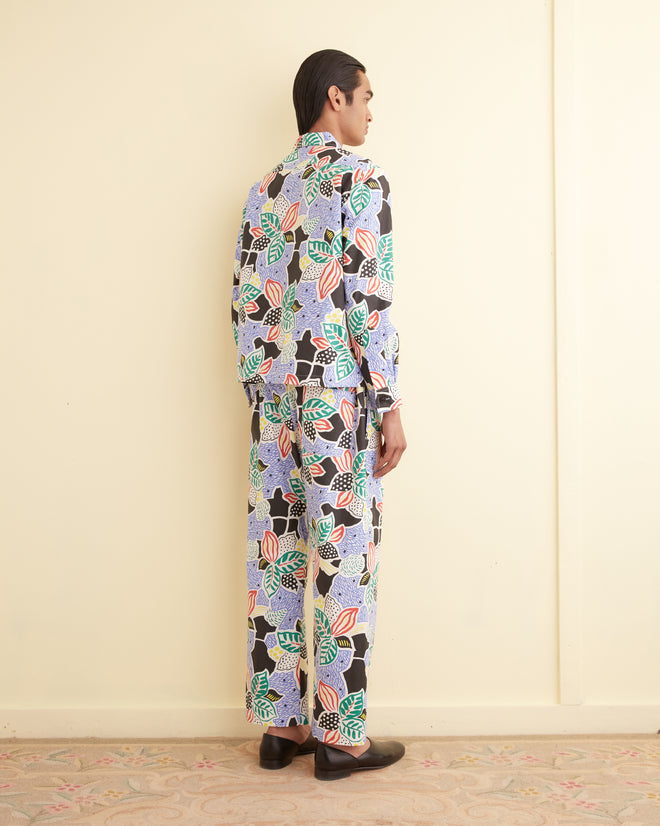 Person stands with back to camera, wearing the Plantain Jazz Long Sleeve Shirt in a unique botanical pattern and black shoes, set against a cream wall.