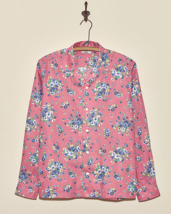 The Plum Shower Shirt is a long-sleeve vintage top in pink with a blue and white floral pattern, displayed hanging on a wall.