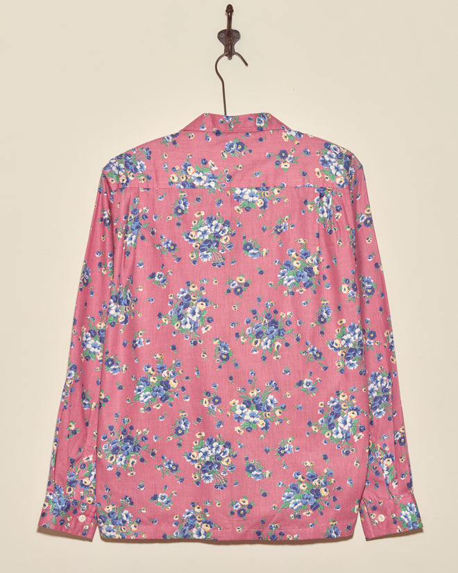 The Plum Shower Shirt is a vintage pink long-sleeve top with a blue and white floral pattern, displayed on a wall hook—a unique, one-of-a-kind piece.