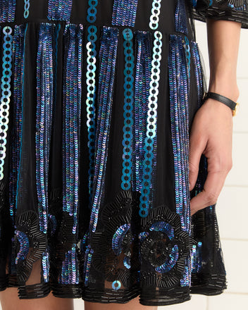 Close-up of a Sequin Podium Dress, a black Art Deco design adorned with blue sequins and intricate patterns, stylishly worn by someone accessorizing with a black watch.