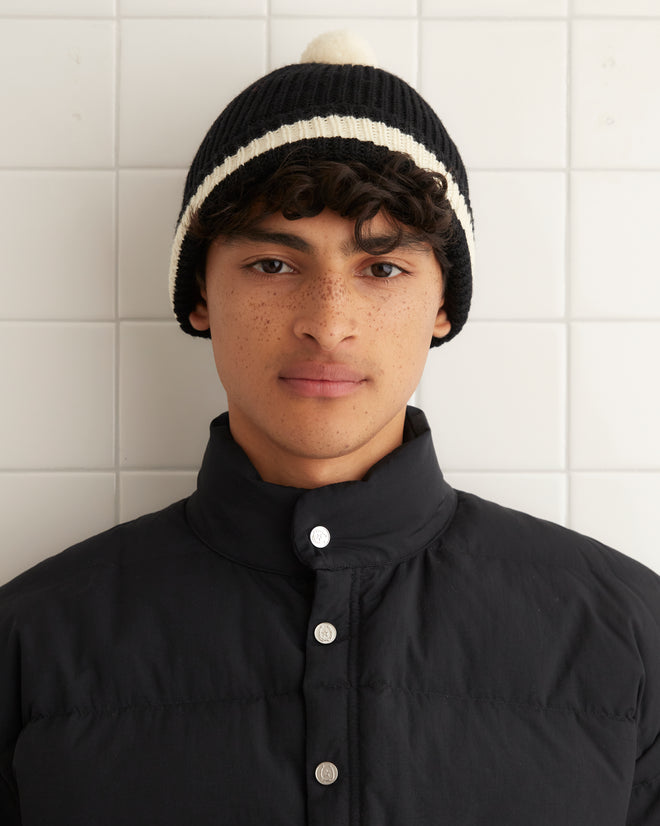 Pom Hat - Black with white stripes, styled in a vintage 1960s-1970s fashion and featuring a pom-pom, displayed against a tiled background.