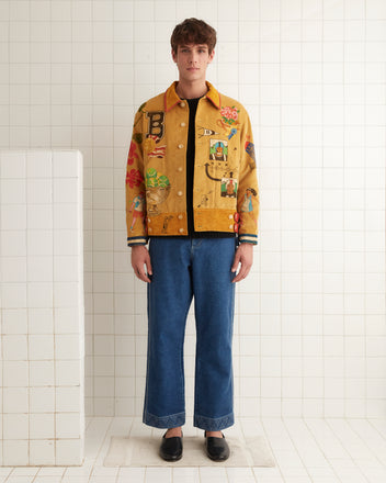 A person wearing a vibrant Bode Recreation Senior Cord Side Tab Jacket, embellished with personalized motifs, stands against a tiled wall in a well-lit room.