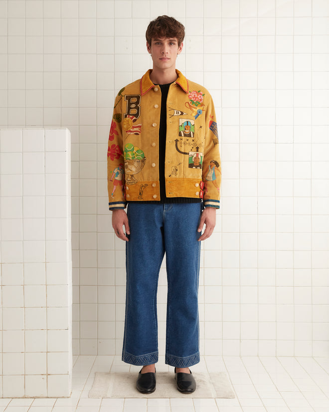 A person wearing a vibrant Bode Recreation Senior Cord Side Tab Jacket, embellished with personalized motifs, stands against a tiled wall in a well-lit room.