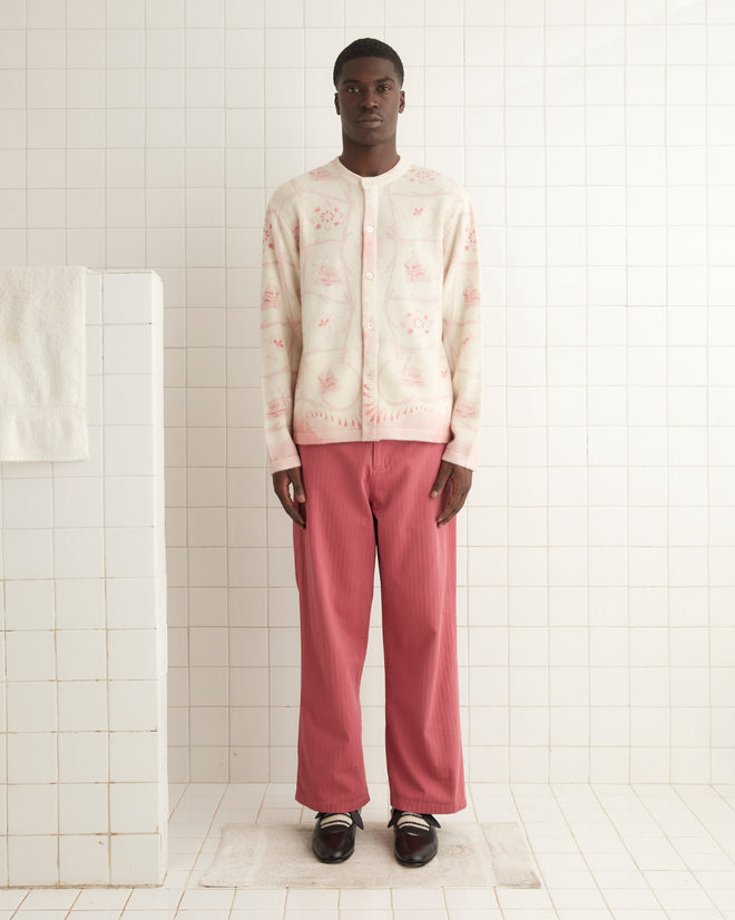 A person stands against a tiled wall, wearing a Printed Mill Cardigan with a floral pattern and pink pants. They have dark shoes on a white tiled floor.