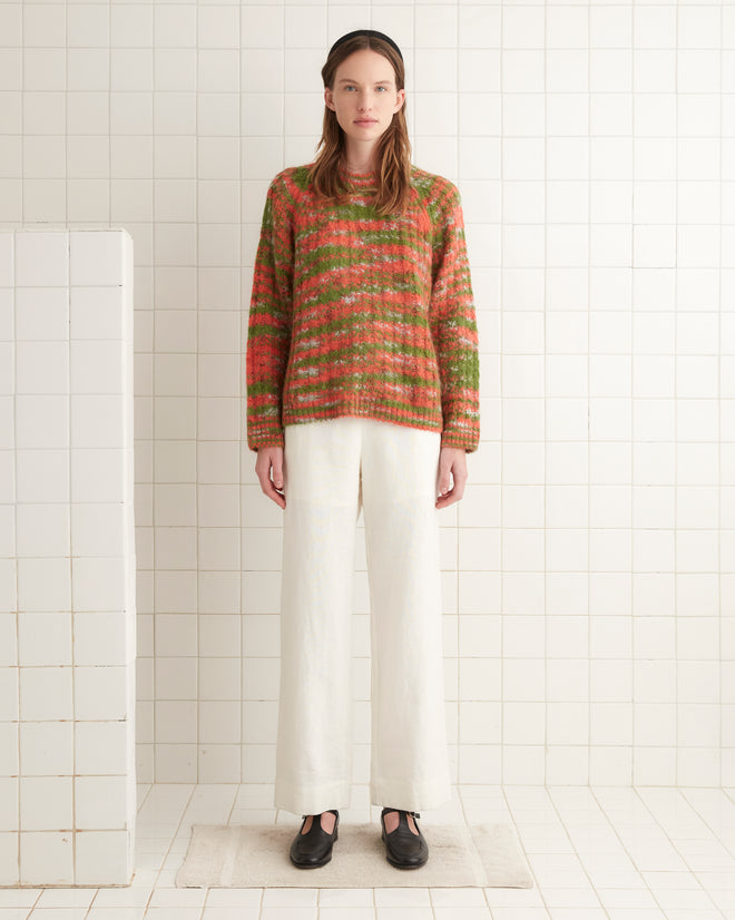 A person wearing a Prismatic Sweater and white pants stands in a tiled room on a beige rug.