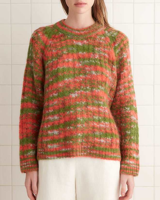 A person wearing a Prismatic Sweater and white pants stands in a tiled room on a beige rug.