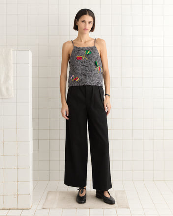 Wearing a Promenade Tank with black pants, embodying sportswear flair, an individual stands in a tiled room with a towel on the wall.