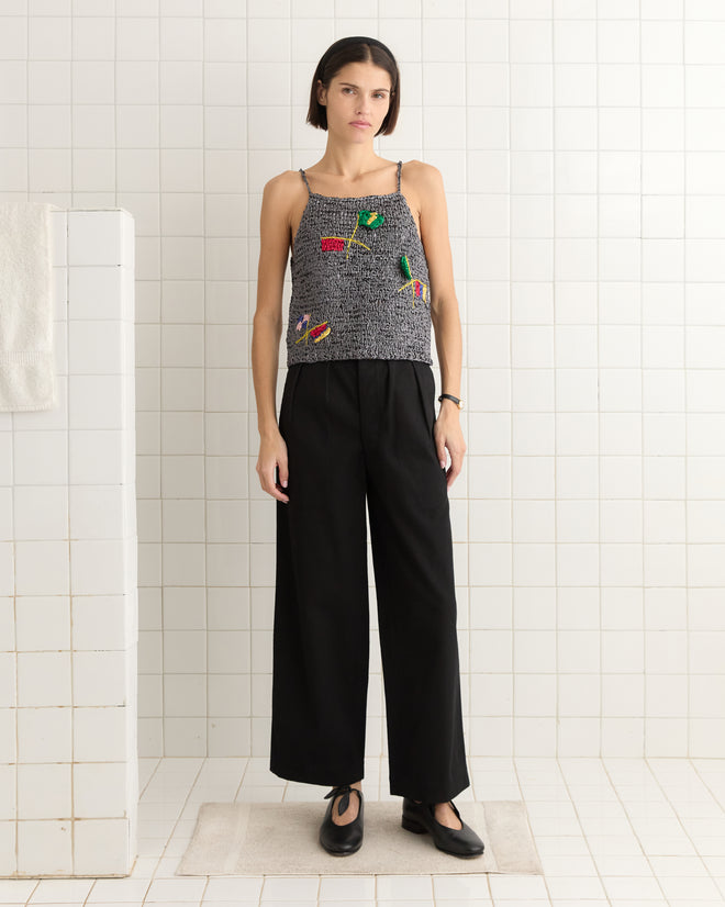 A person in a tiled room wears the Promenade Tank from a renowned sportswear label and black pants, standing on a mat with hands by their sides.
